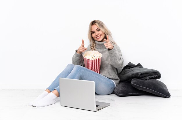 Tiener blonde meisje popcorn eten tijdens het kijken naar een film op de laptop