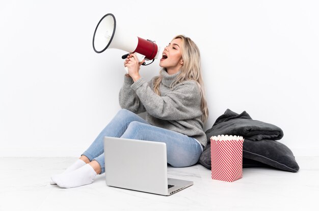 Tiener blondevrouw die popcorn eten terwijl het letten van op een film op laptop die door een megafoon schreeuwt