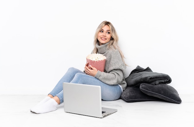 Tiener blondevrouw die popcorn eten terwijl het letten van op een film op laptop met gekruiste en gelukkige wapens