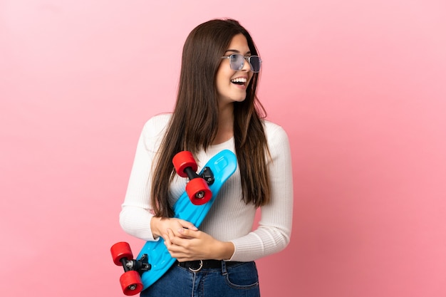 Tiener Braziliaans meisje over geïsoleerde achtergrond met een skate met gelukkige uitdrukking