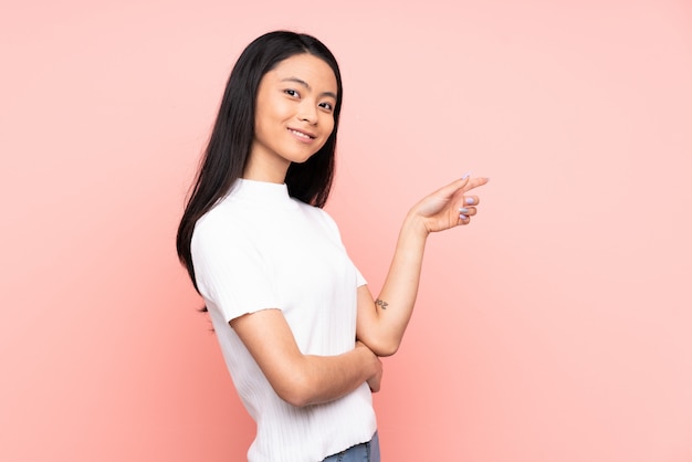 Tiener Chinese vrouw die op roze achtergrond wordt geïsoleerd die vinger aan de kant richt