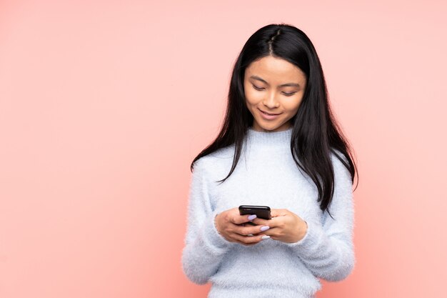 Tiener Chinese vrouw die op roze muur een bericht met mobiel verzendt