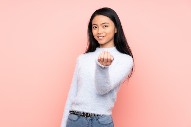 Tiener Chinese vrouw die op roze muur wordt geïsoleerd die met hand uitnodigt te komen. Blij dat je bent gekomen