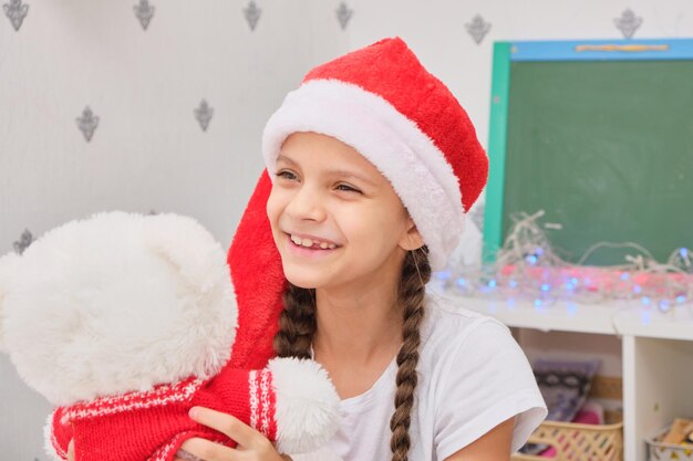 Tiener cite meisje knuffelt witte teddybeer in rode trui, meisje in met kerst versierde kamer
