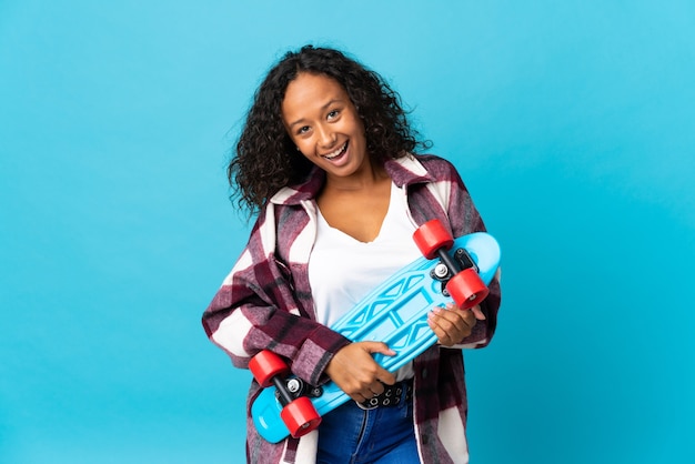 Tiener Cubaans meisje geïsoleerd op blauwe muur met een skate met gelukkige uitdrukking