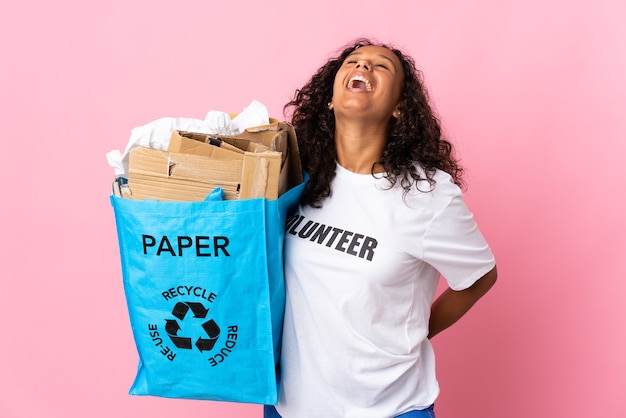 Tiener Cubaans meisje met een recycling zak vol papier om te recyclen geïsoleerd op roze achtergrond lachen