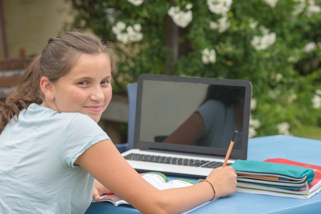 Tiener die haar thuiswerk met laptop in de tuin doet