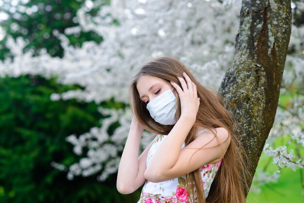 Tiener die het masker van de beschermingsgeneeskunde in bloeiende tuin draagt