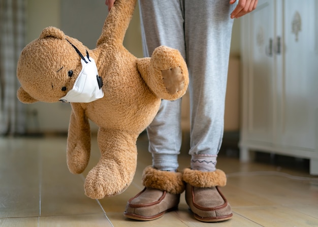 Tiener die teddybeer met gezichtsmasker koestert.