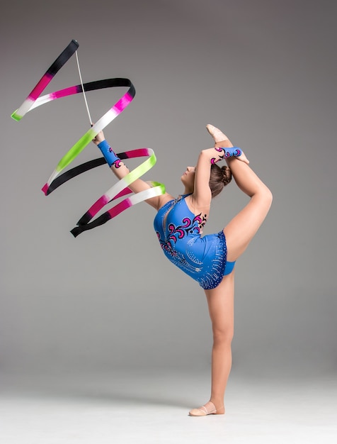 Foto tiener doet gymnastiekdans met gekleurd lint op een grijze achtergrond