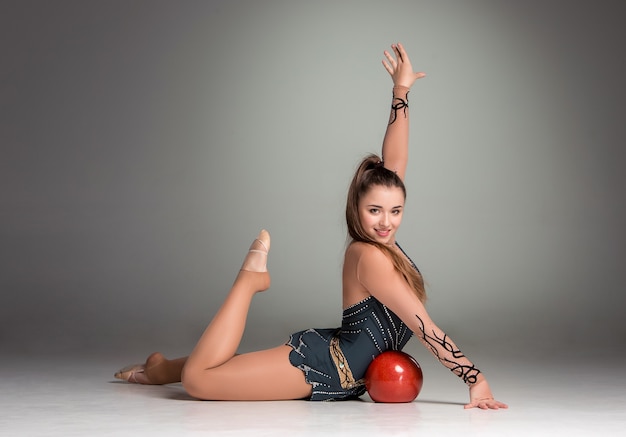 Tiener doet gymnastiekoefeningen met rode gymnastiekbal op een grijze achtergrond