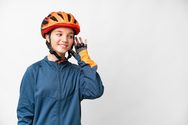 Tiener fietser meisje over geïsoleerde witte achtergrond luisteren naar iets door de hand op het oor te leggen