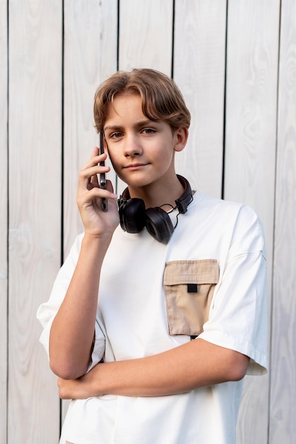 Foto tiener jongen praat op een mobiele telefoon buiten op een witte houten achtergrond