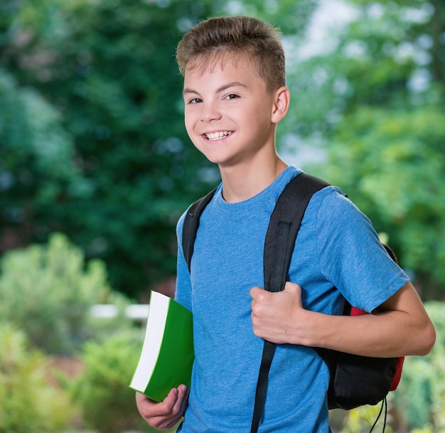 Foto tiener jongen van 12-14 jaar met schooltas en boek die buiten poseert