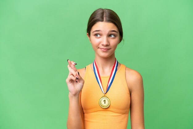 Tiener kaukasisch meisje met medailles over geïsoleerde achtergrond met gekruiste vingers en het beste wensen