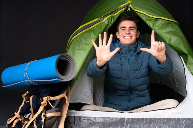 Tiener Kaukasische mens binnen een het kamperen groene tent op zwarte muur die zeven met vingers tellen