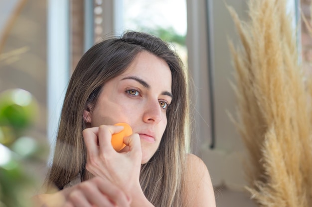 Tiener kijkt naar de spiegel en doet de basis van haar make-up met een blender