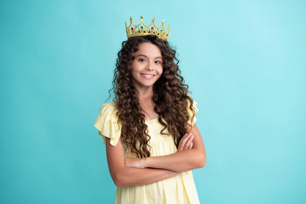 Tiener kind in koningin kroon geïsoleerd op blauwe achtergrond Prinses meisje in tiara Tienermeisje slijtage diadeem Gelukkig tiener positieve en lachende emoties van tiener meisje