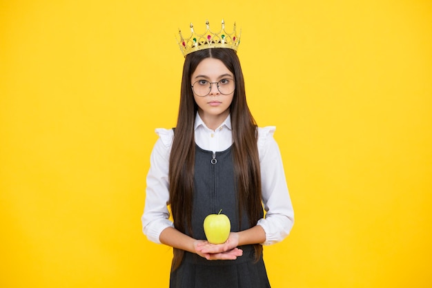 Tiener kind in koningin kroon houden appel geïsoleerd op gele achtergrond Prinses meisje in tiara Teenage meisje slijtage diadeem