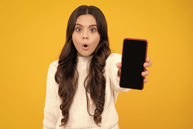 Tiener kind meisje met smartphone Hipster meisje met mobiele telefoon Verrast tienermeisje Kid weergegeven: leeg scherm mobiele telefoon mock up kopie ruimte