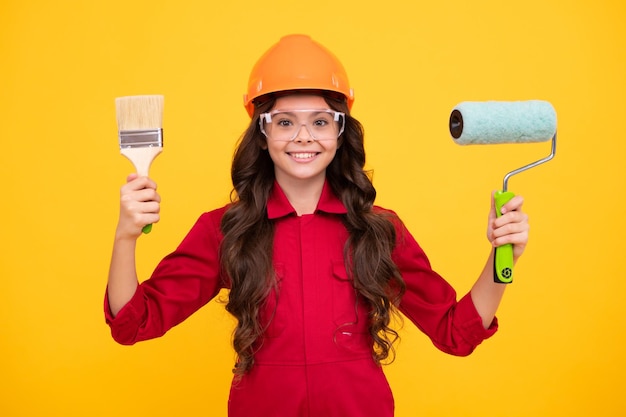 Tiener kind schilder in helm met penseel Kind in harde hoed Kid bouwer schilder op bouwplaats Renovatie en reparatie Gelukkig lachende emoties van tiener meisje