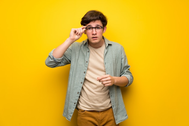 Tiener man over gele muur met een bril en verrast