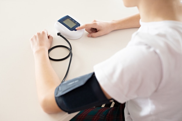 Tiener meet bloeddruk met monitor in huis.