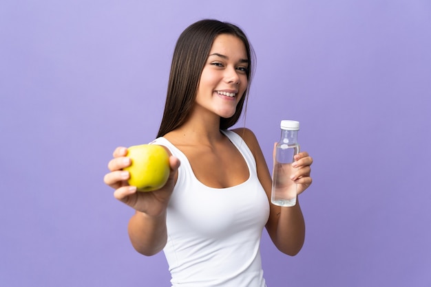 Tiener meisje geïsoleerd op paars met een appel en met een fles water