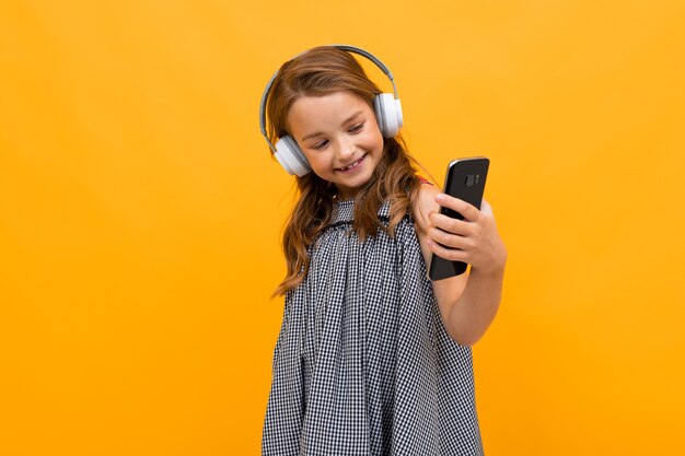 Tiener meisje geniet van muziek op koptelefoons en dansen op een gele achtergrond met kopie ruimte.