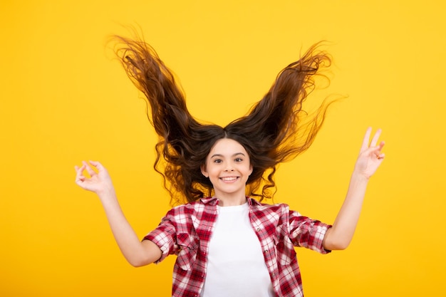 Tiener portret met gekke beweging haar Jonge tiener kind met wapperende haren Brunette tiener meisje fladderende haren in beweging geïsoleerd op gele achtergrond