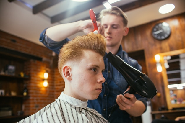 Tiener roodharige jongen kapsels kapper in de kapper. modieus stijlvol retro kapsel. portret van een kind met een mooi kapsel. ,