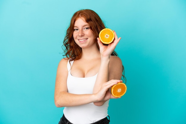Tiener roodharige meisje geïsoleerd op blauwe achtergrond in zwembroek en houden een sinaasappel