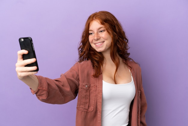 Tiener roodharige meisje over geïsoleerde paarse achtergrond maken een selfie