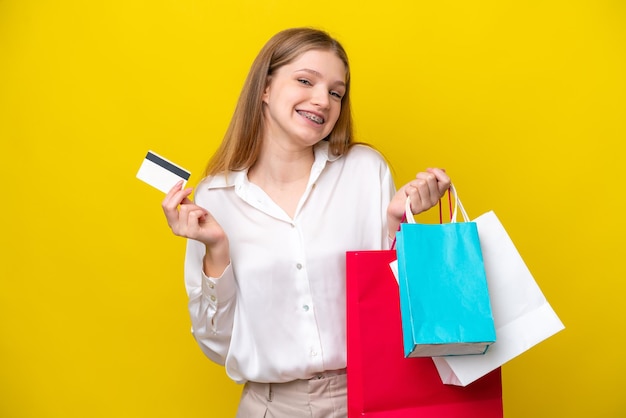 Tiener Russisch meisje geïsoleerd op gele achtergrond met boodschappentassen en een creditcard