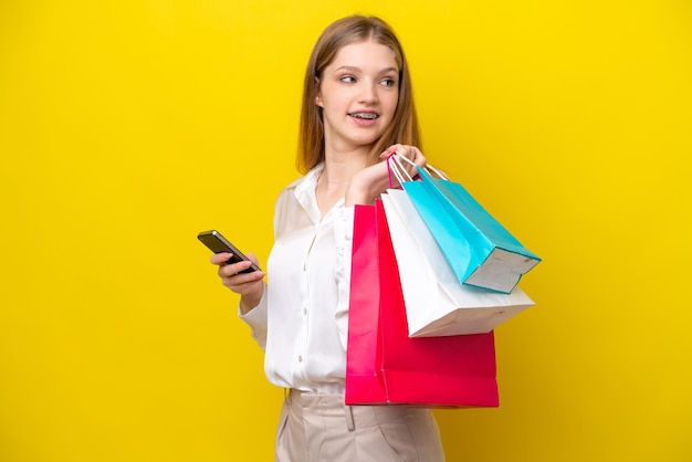 Tiener Russisch meisje geïsoleerd op gele achtergrond met boodschappentassen en een mobiele telefoon