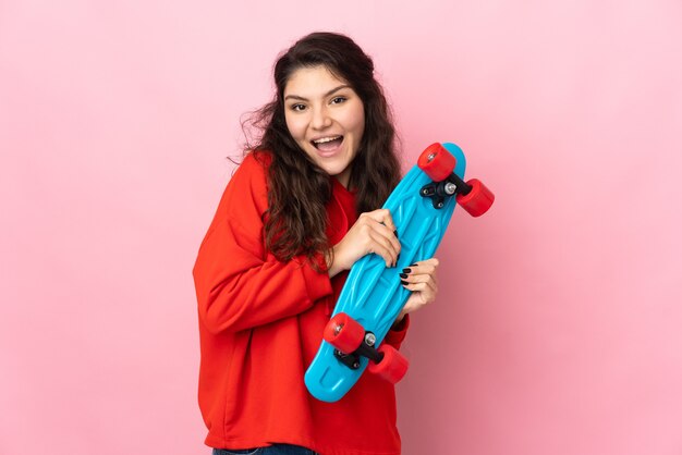 Tiener Russisch meisje geïsoleerd op roze achtergrond met een skate met gelukkige uitdrukking