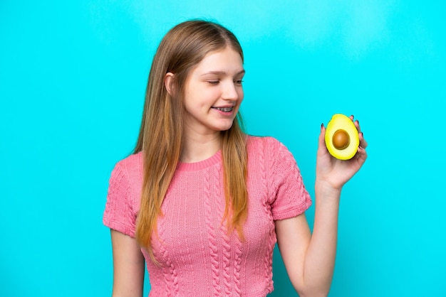 Tiener Russisch meisje met een avocado geïsoleerd op blauwe achtergrond met gelukkige expressie