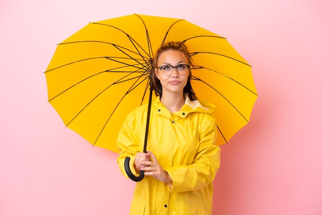 Tiener Russisch meisje met regenbestendige jas en paraplu geïsoleerd op roze achtergrond en opzoeken