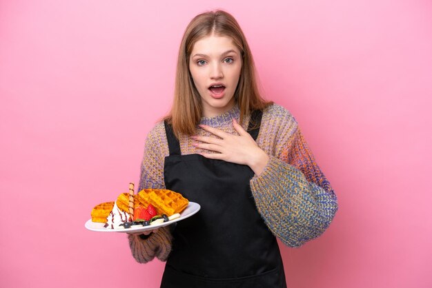 Tiener Russisch meisje met wafels geïsoleerd op roze achtergrond verrast en geschokt terwijl ze naar rechts kijkt