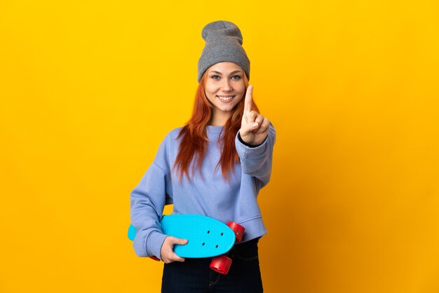 Tiener Russisch skater meisje geïsoleerd op een gele achtergrond die een vinger toont en optilt