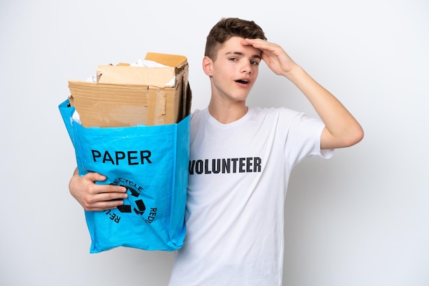 Tiener russische man met een recyclingzak vol papier om te recyclen geïsoleerd op een witte achtergrond en doet een verrassingsgebaar terwijl hij naar de zijkant kijkt