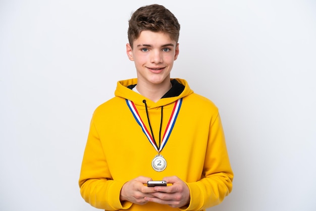 Tiener Russische man met medailles geïsoleerd op een witte achtergrond die een bericht verzendt met de mobiel