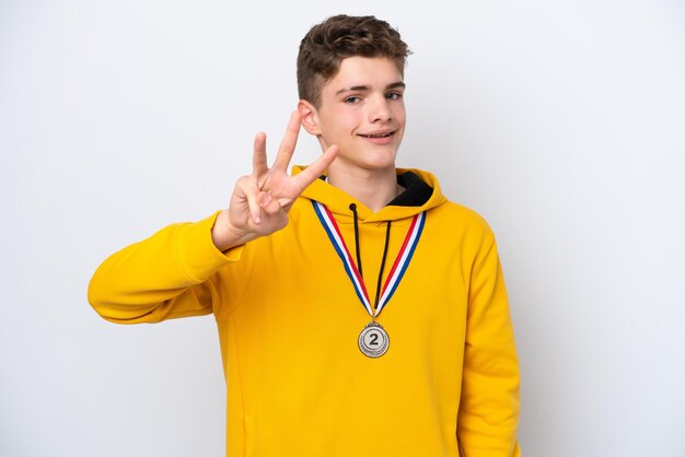 Tiener Russische man met medailles geïsoleerd op een witte achtergrond gelukkig en drie tellen met vingers