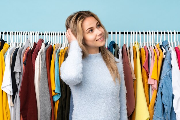 Tiener Russische vrouw die sommige kleren kopen die op blauwe muur worden geïsoleerd die een idee denken