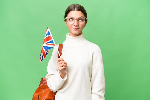 Tiener student blank meisje houdt een vlag van het Verenigd Koninkrijk over geïsoleerde achtergrond en kijkt omhoog