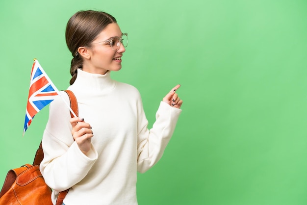 Tiener student blank meisje met een vlag van het Verenigd Koninkrijk over geïsoleerde achtergrond wijzende vinger naar de zijkant en een product presenteren