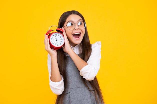 Tiener student meisje houdt klok geïsoleerd op gele achtergrond Tijd naar school Tiener kind met wekker toont tijd laat ontwaken Gelukkig gezicht positieve en lachende emoties van tiener meisje