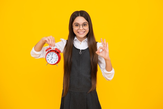 Tiener student meisje houdt klok geïsoleerd op gele achtergrond Tijd naar school Tiener kind met wekker toont tijd laat ontwaken Gelukkig meisje gezicht positieve en lachende emoties