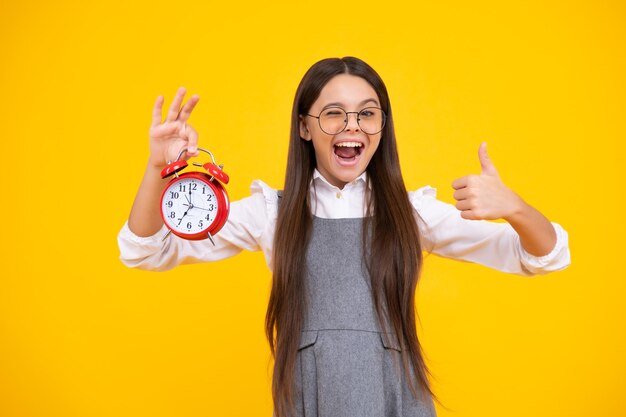 Tiener student meisje houdt klok geïsoleerd op gele achtergrond tijd naar school tiener kind met wekker weergegeven: tijd laat ontwaken Opgewonden tiener meisje