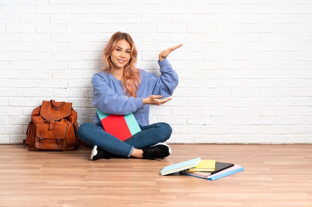 Tiener student vrouw met roze haar zittend op de vloer binnenshuis copyspace te houden om een advertentie in te voegen